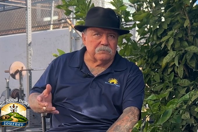 Eddie Blajos in a black hat and navy polo, seated outdoors during an interview.